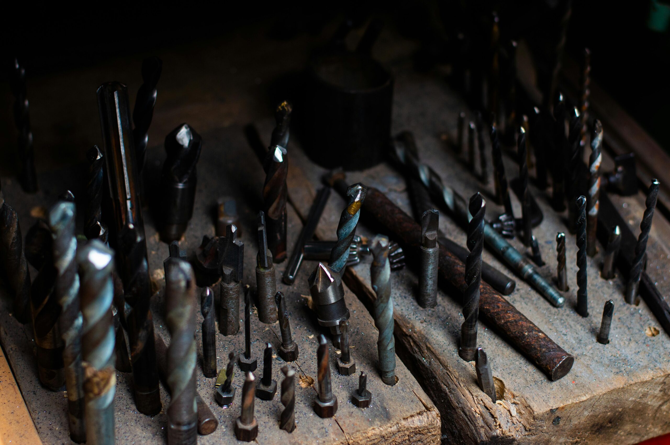Collection of various drill bits on a wooden board, ideal for metalwork and woodworking.